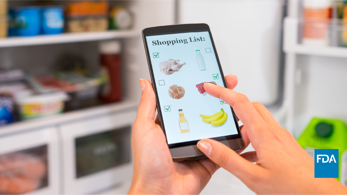 Person uses grocery shopping list on mobile phone while standing in front of refrigerator