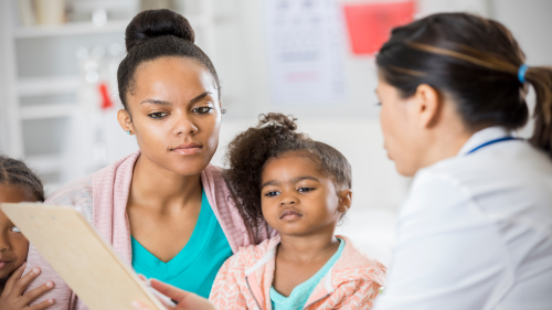 Mother and doctor reviewing an informed consent form while young daughter looks on 