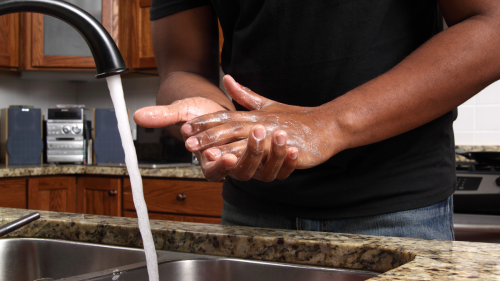 man washing hands with soap and water at kitchen sink
