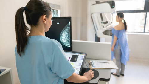 a nurse giving a patient a mammogram including the image of the patient's breast on the computer monitor