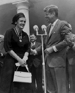 Frances Kelsey standing in front of microphones with President John F. Kennedy, with a medal around her neck