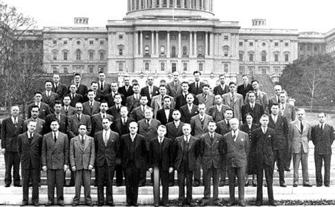 Group picture of men in suits, standing in front of the U.S. Capitol