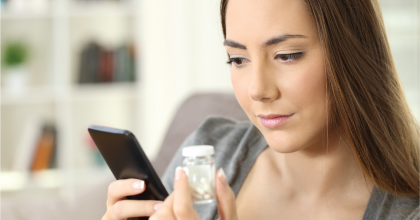Woman holding a phone and a bottle of medication
