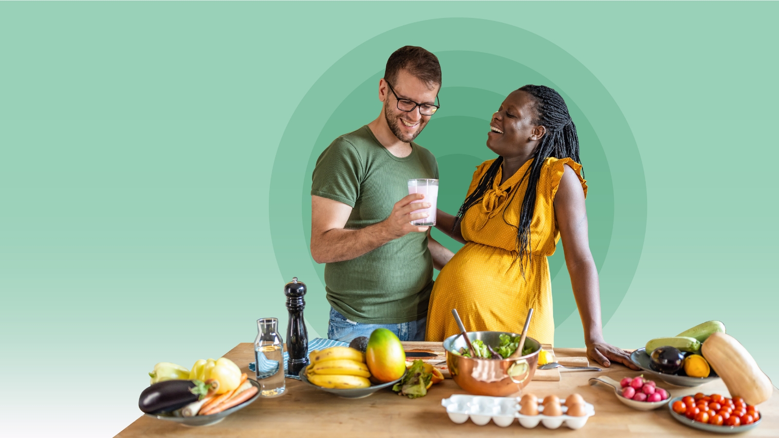 Image of pregnant woman with partner standing in front of a table with a spread of healthy food items