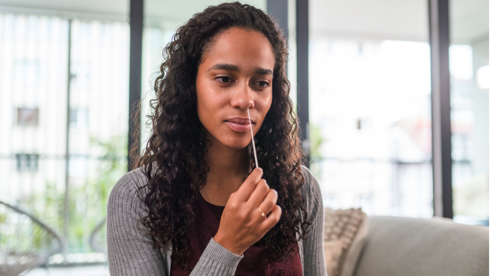 A woman performing a nose swab on herself as part of a COVID at home test