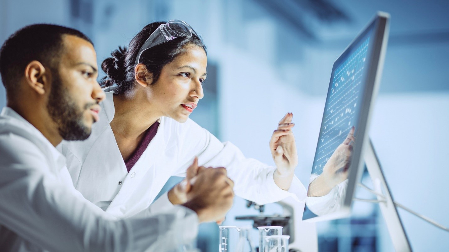 Two scientists in white coats looking at a screen.