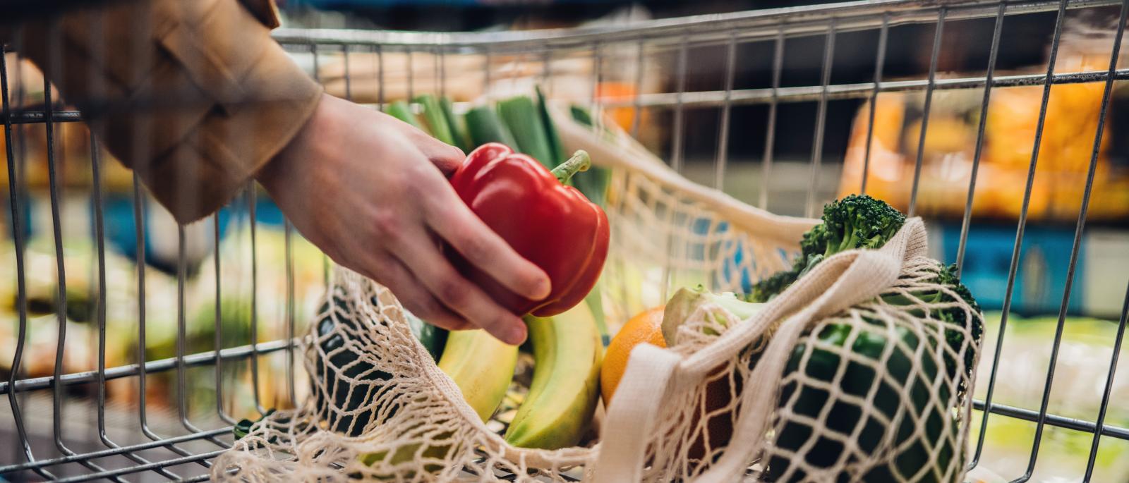 Shopper picking fruits and vegetables in a grocery store and putting them in a cart