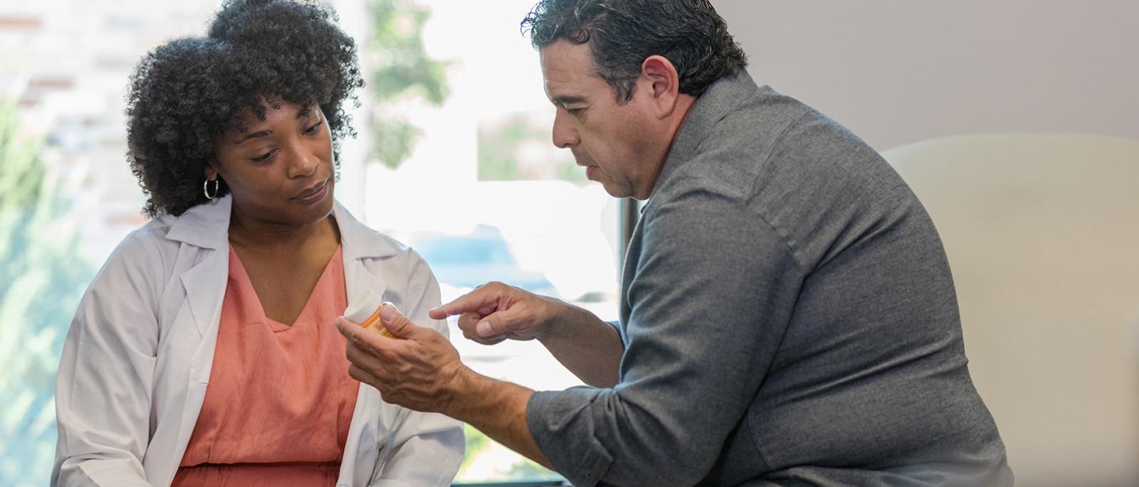 Male patient points to pill bottle while talking to doctor.