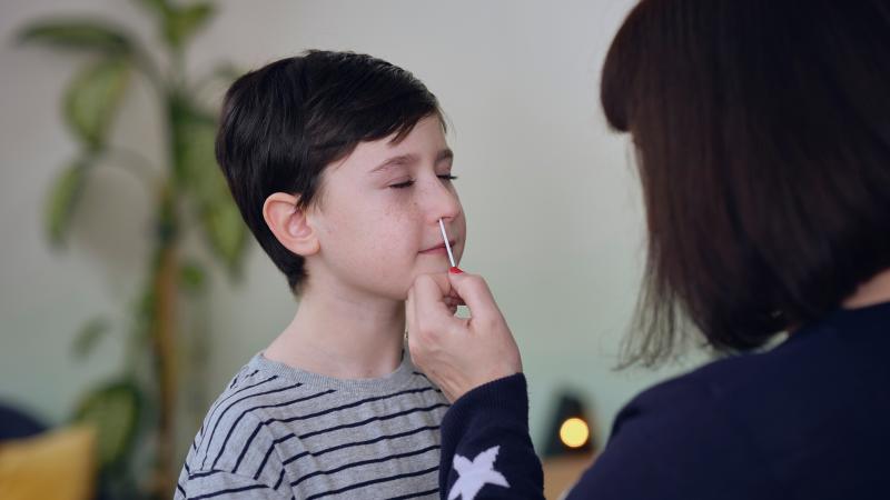Adult taking a sample from a child's nose for a COVID-19 at-home test.