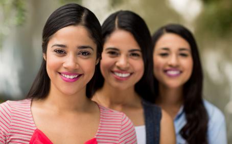 Three young Hispanic women smiling at the camera with focus on the first one