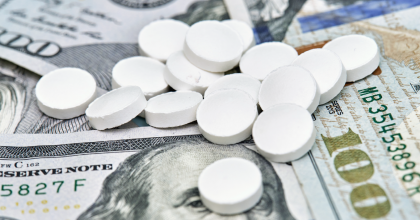 A handful of pills on top of a group of 100-dollar bills