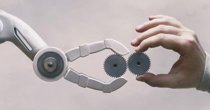 Robot arm and human hand meet, with gears, representing the concept of advanced manufacturing