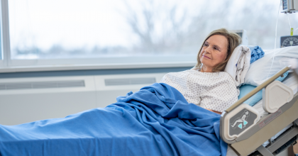 A female patient in a hospital gown rests in a hospital bed.