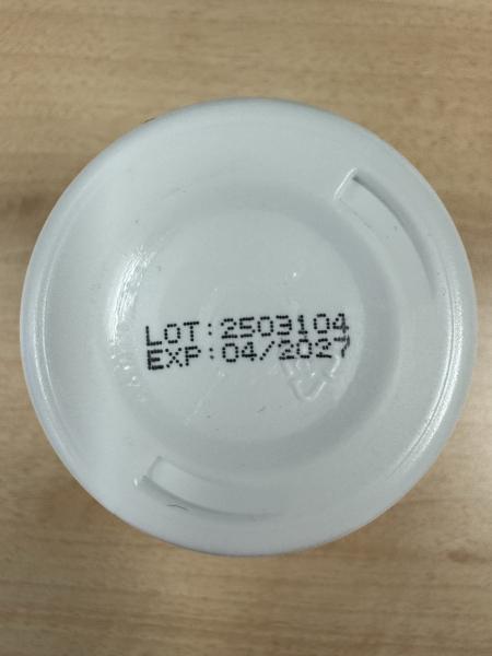 Bottom of a white plastic bottle cap resting on a light wood surface. Printed in black dot-matrix text: LOT: 2503104, EXP: 04/2027