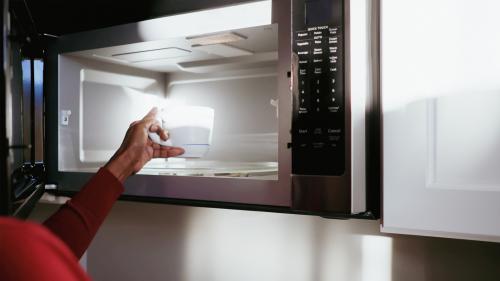 A woman placing a cup into a microwave.